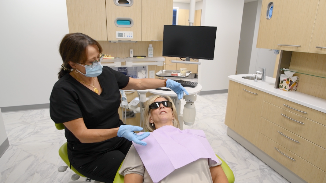 Woman smiling, looking at her teeth in a handheld mirror.