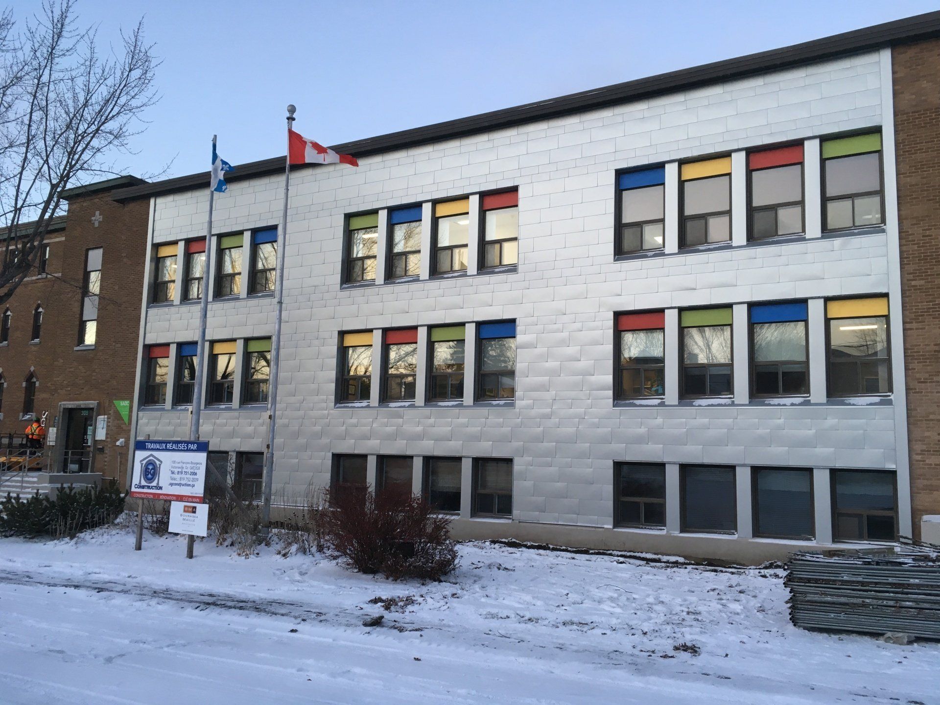 Extérieur d'un bâtiment scolaire sous la neige, encadrements de fenêtres colorés, drapeaux.