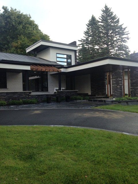 Maison moderne avec bardage foncé, toit noir et pelouse soignée.