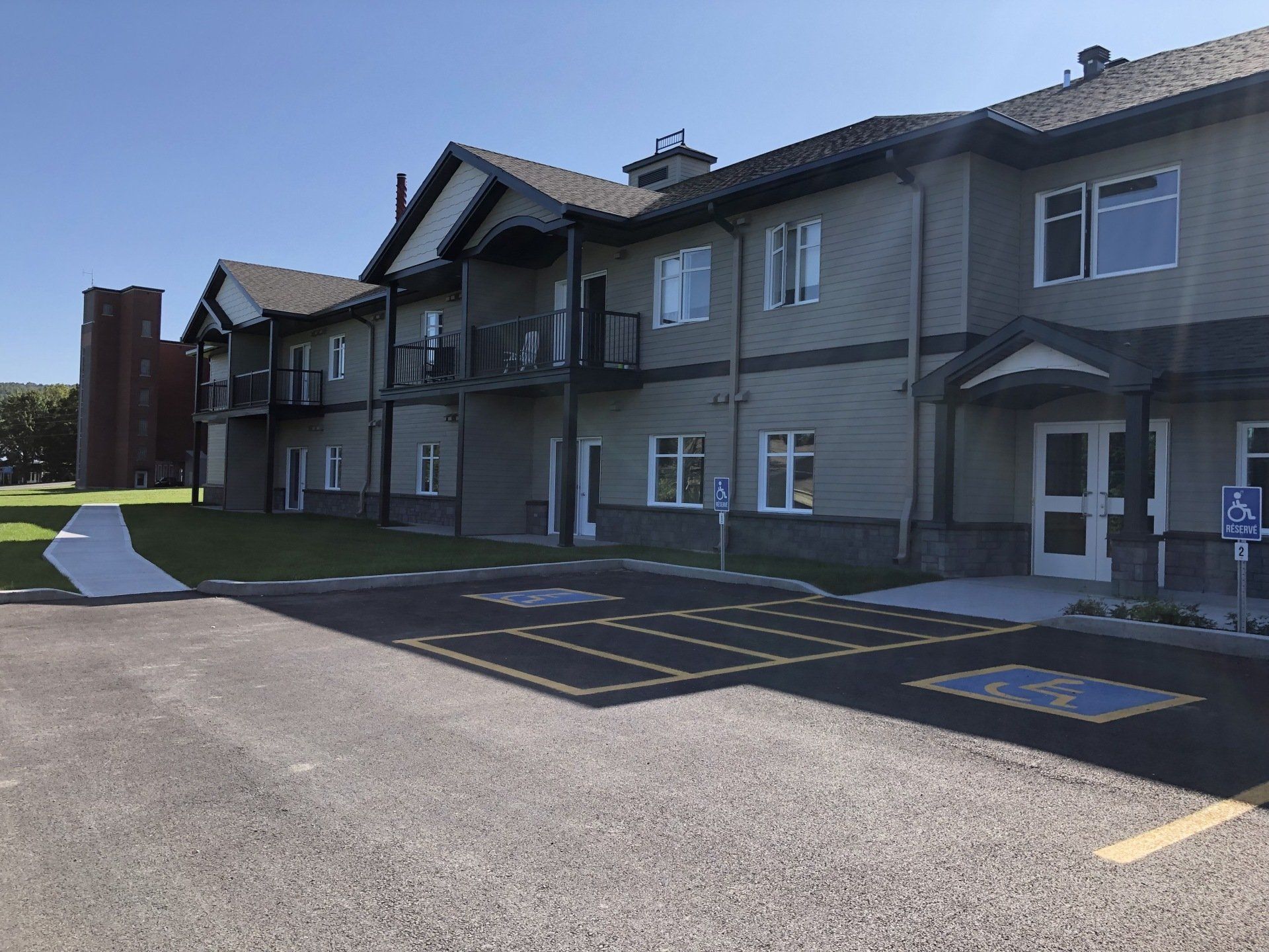 Extérieur d'un bâtiment de deux étages avec places de parking accessibles. Bardage vert, ciel bleu.