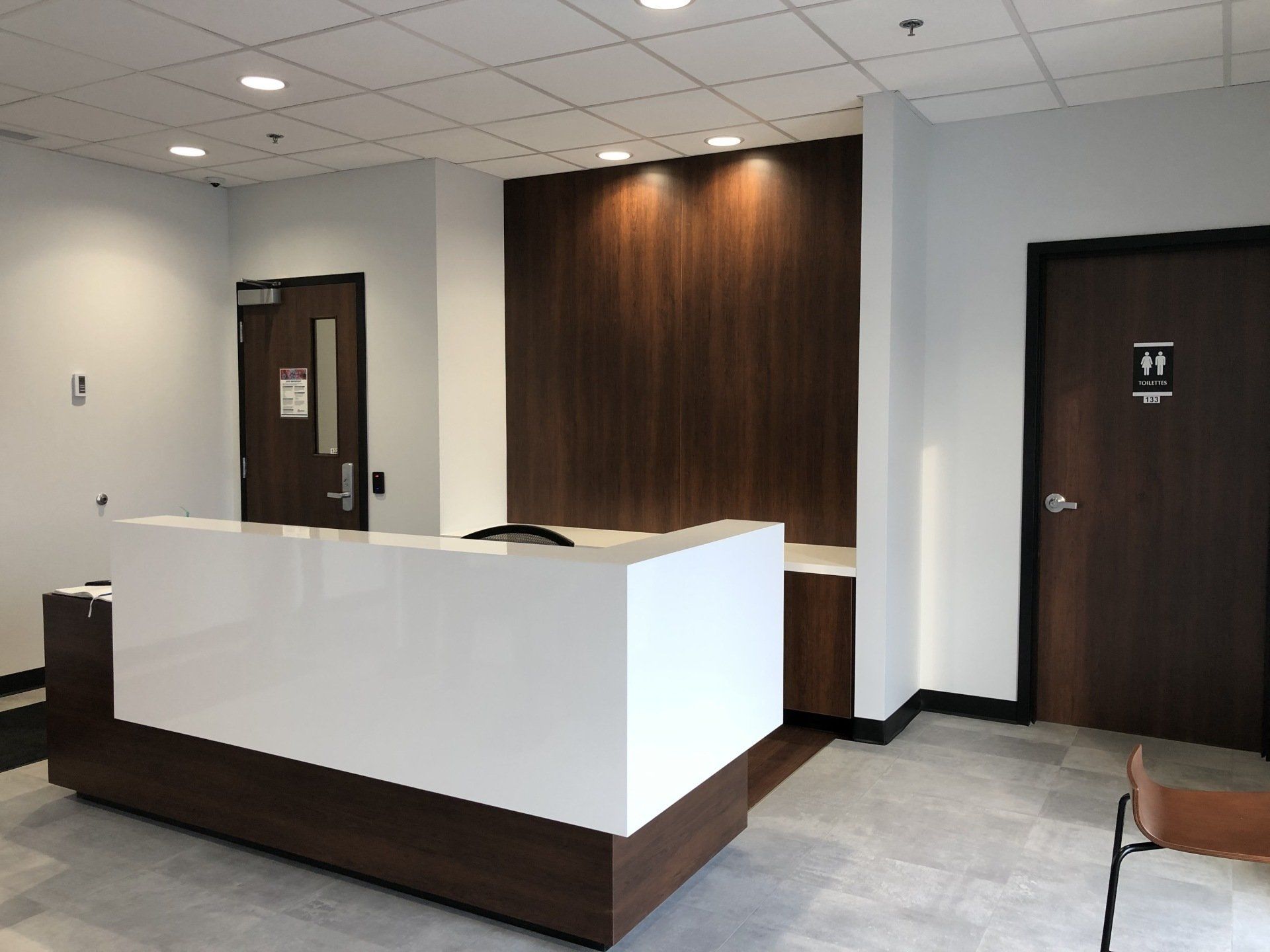 Espace d'accueil moderne avec un comptoir blanc et des boiseries foncées.