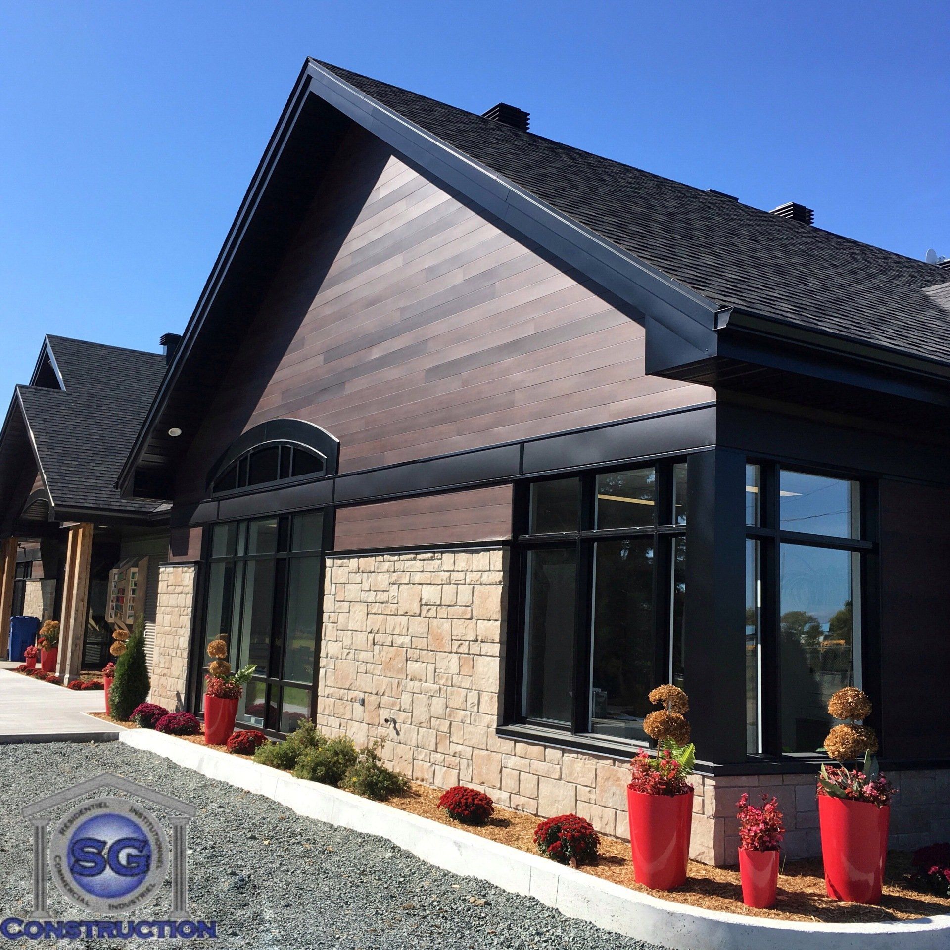 Façade moderne du bâtiment avec revêtement en pierre et en bois foncé, fenêtres à cadre noir et jardinières rouges.