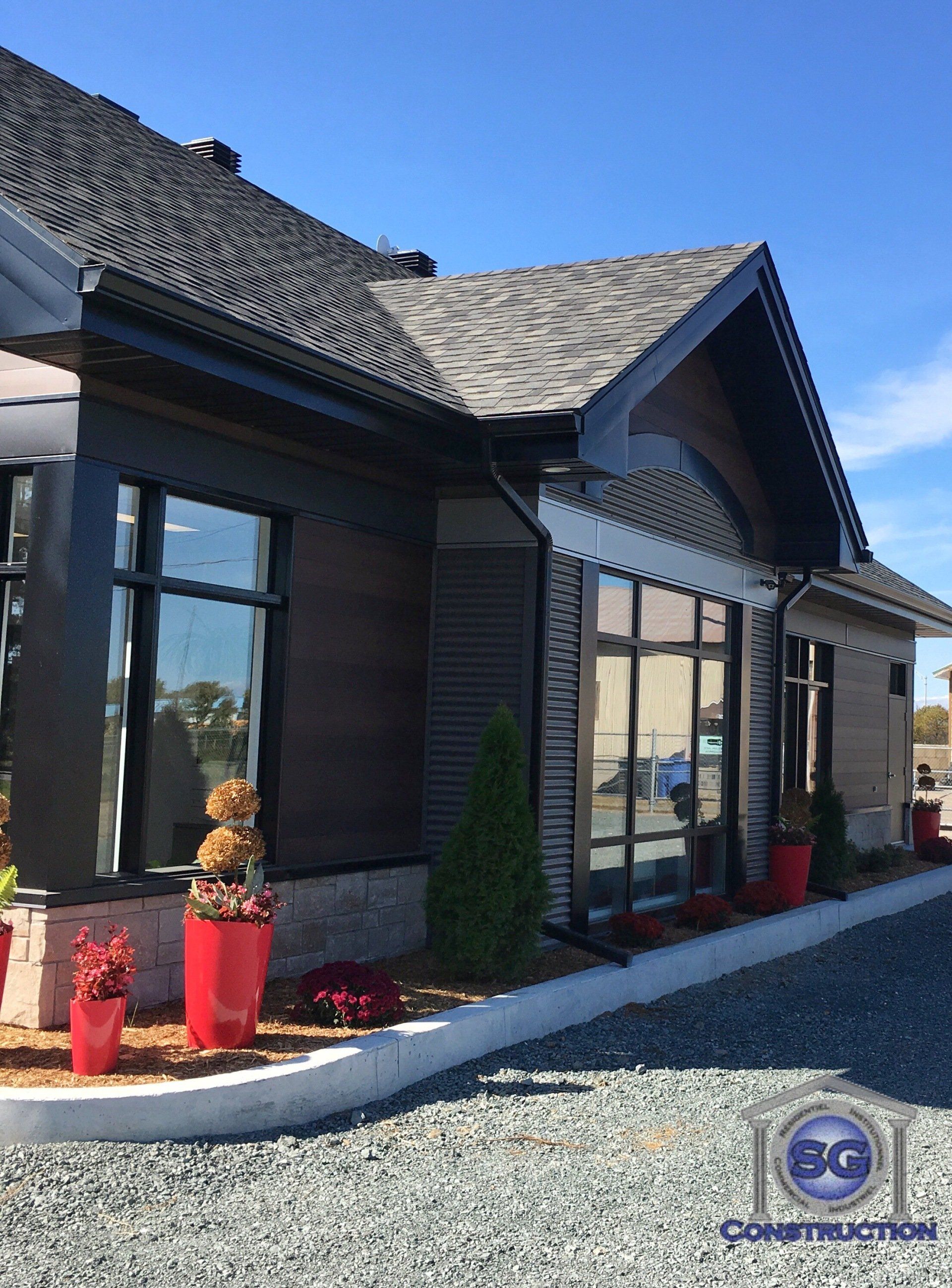 Vue extérieure d'un bâtiment moderne avec un bardage en bois foncé, des fenêtres à cadre noir et des pots de fleurs rouges.