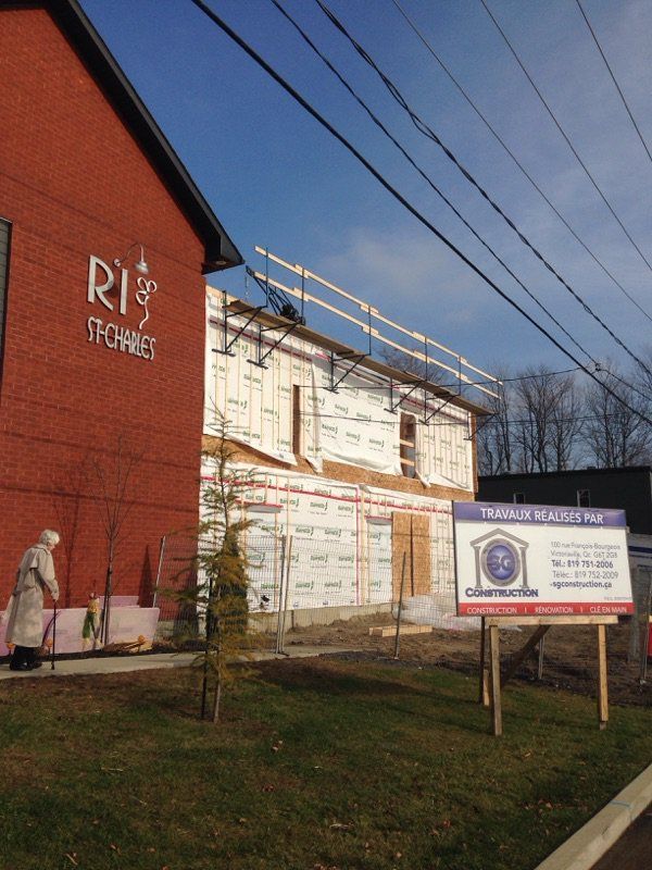 Bâtiment en construction à côté d'un immeuble en briques. Panneau de chantier devant.