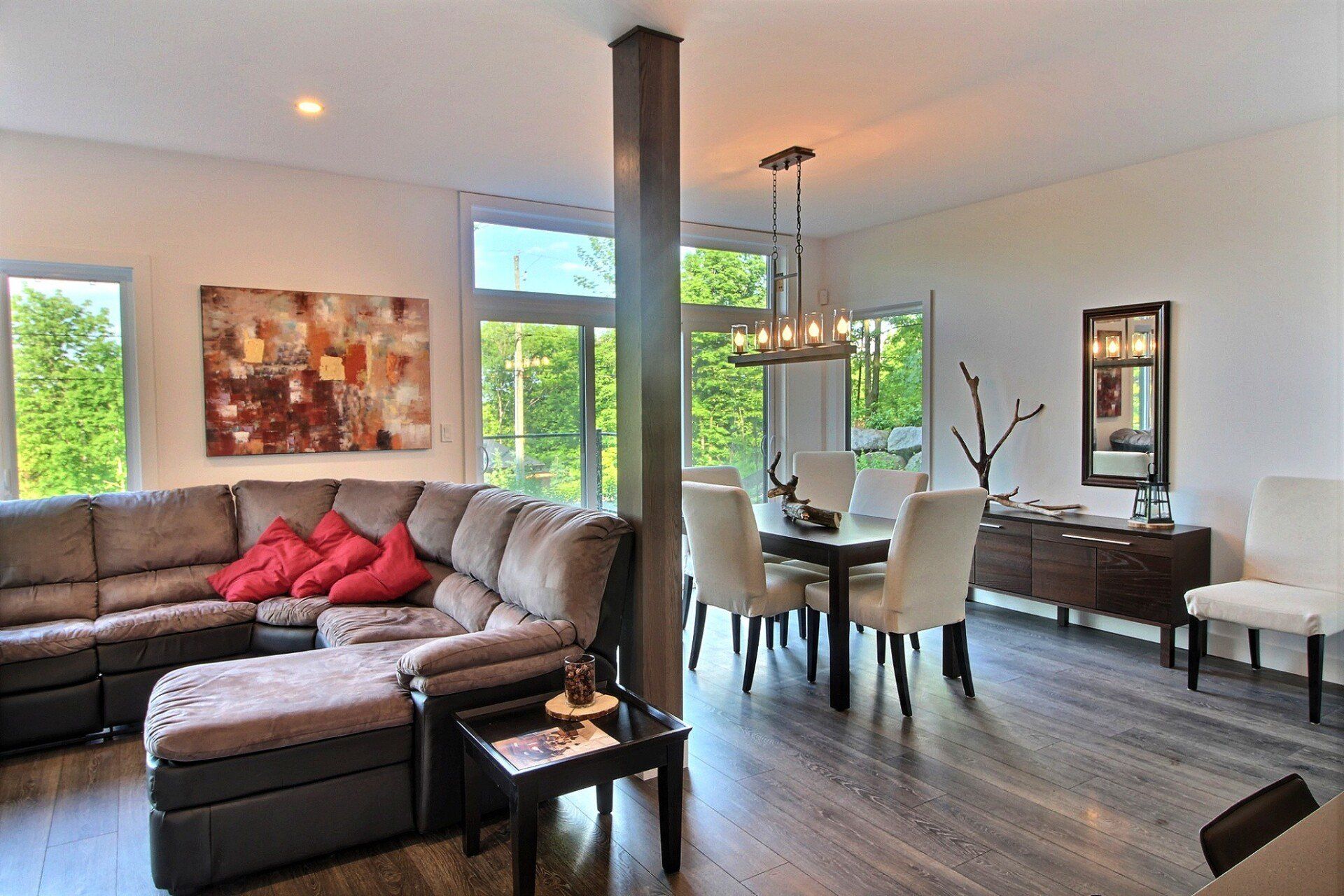 Salon moderne avec canapé d'angle, coin repas, œuvres d'art et lumière naturelle.