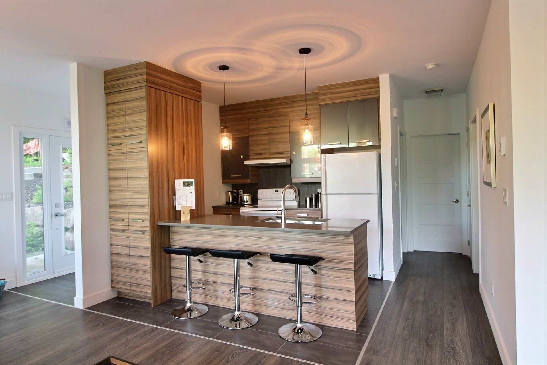 Cuisine moderne avec un bar , appareils électroménagers en acier inoxydable, lambris et suspensions lumineuses.