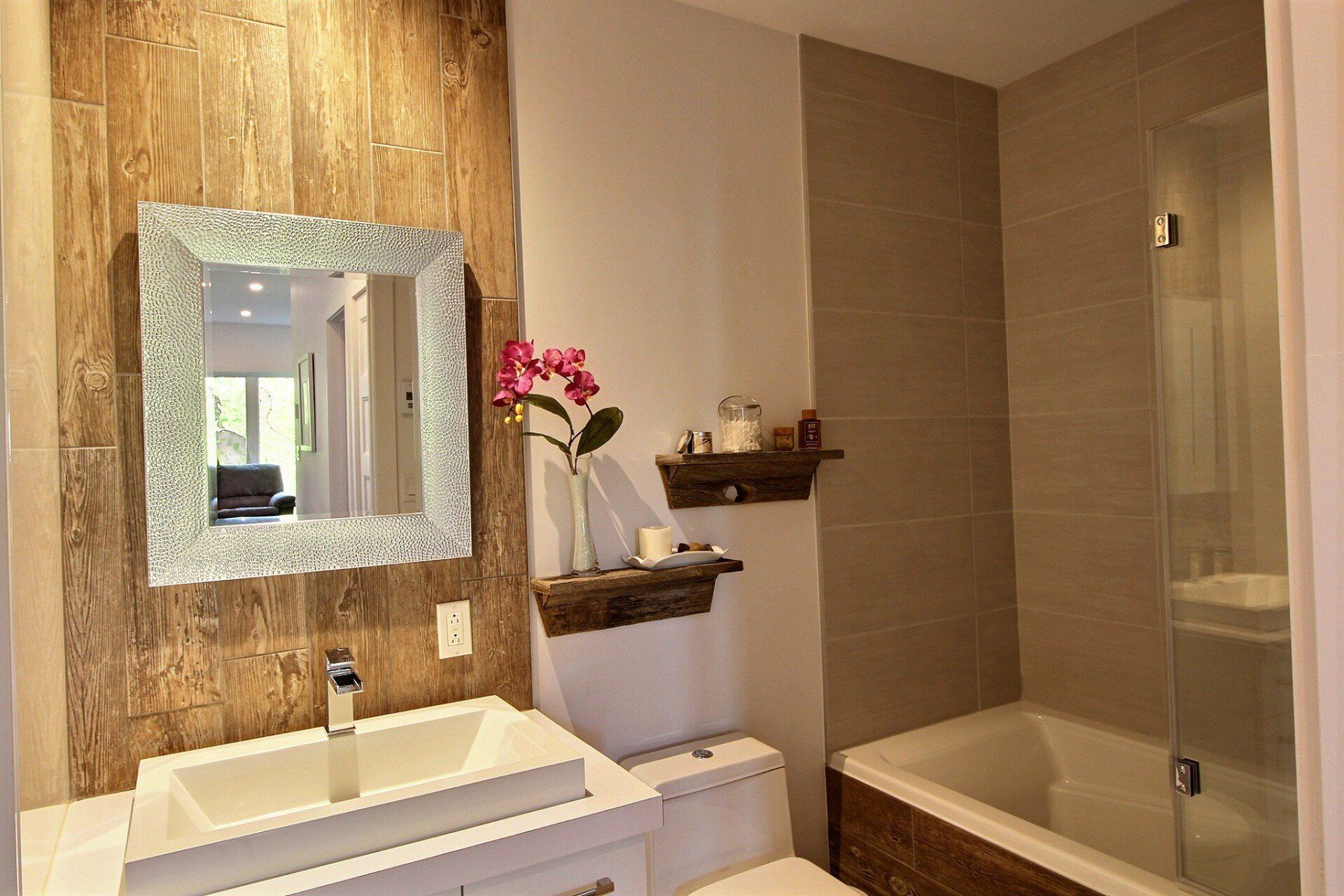 Salle de bains avec mur d'accent imitation bois, meuble-lavabo et toilettes blancs, et cabine de douche en verre.