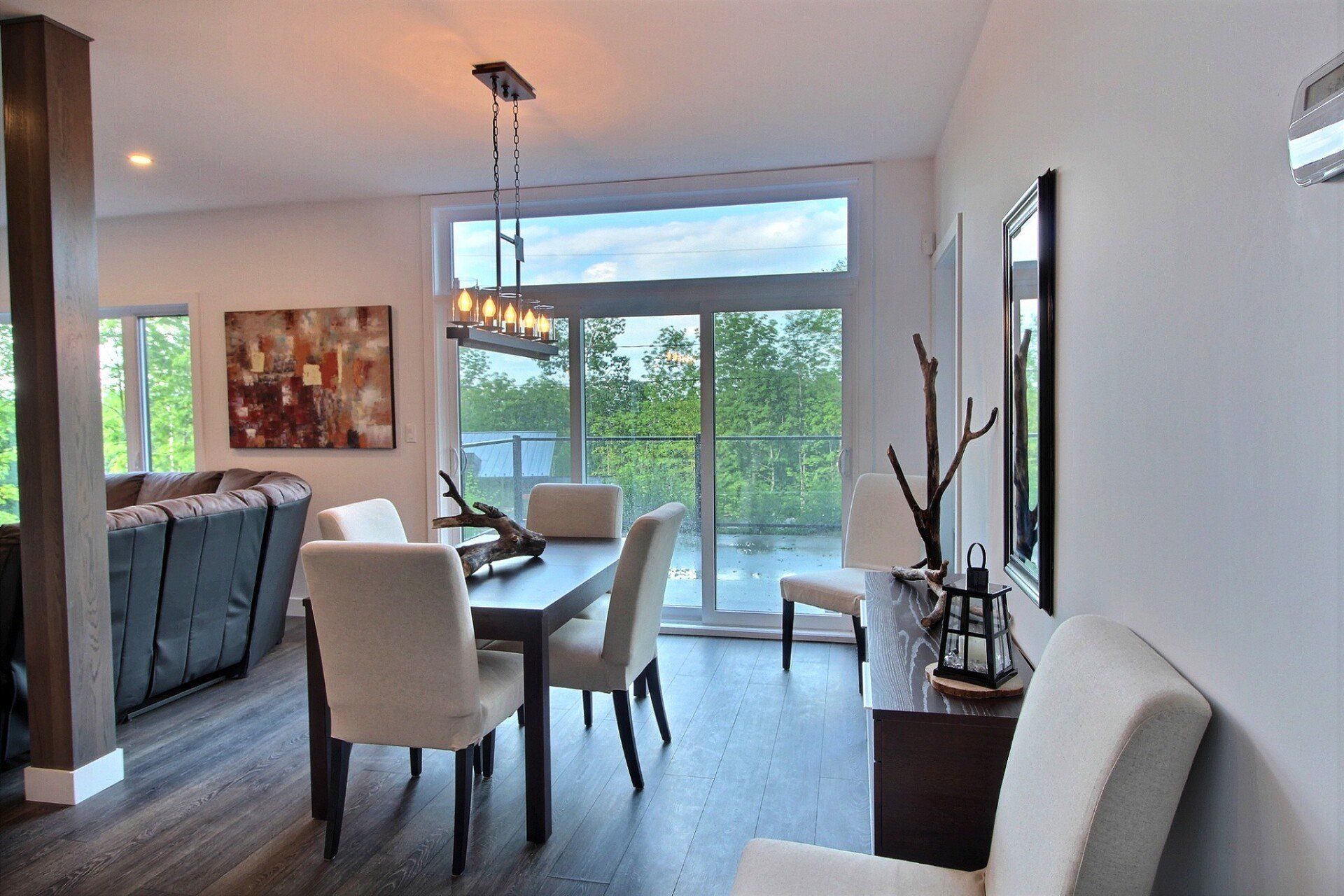 Salle à manger avec table, chaises, œuvres d'art et porte-fenêtre coulissante. Parquet foncé et murs clairs.