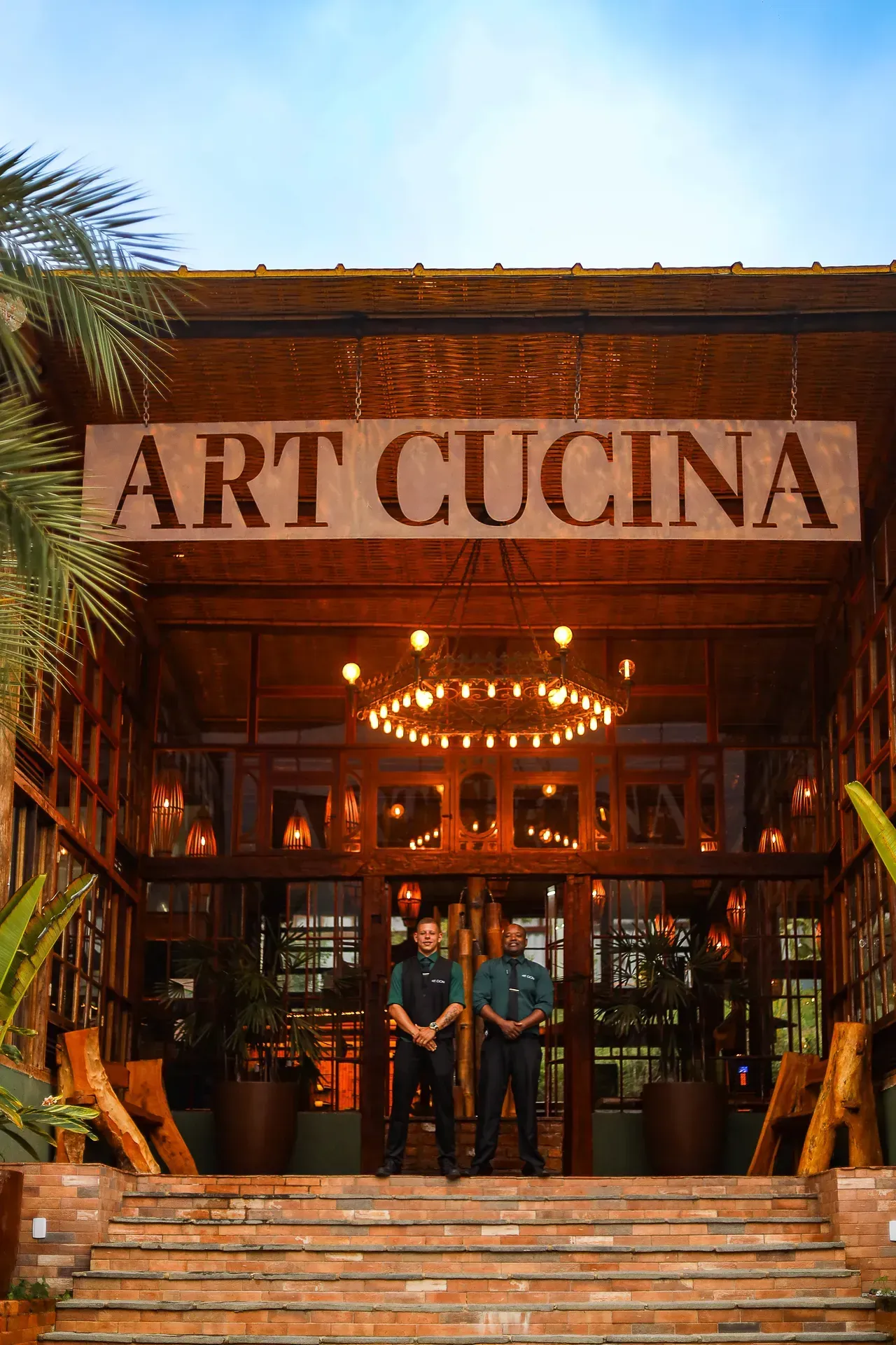 Entrada do restaurante ART CUCINA com luzes aconchegantes e duas pessoas em pé na porta.
