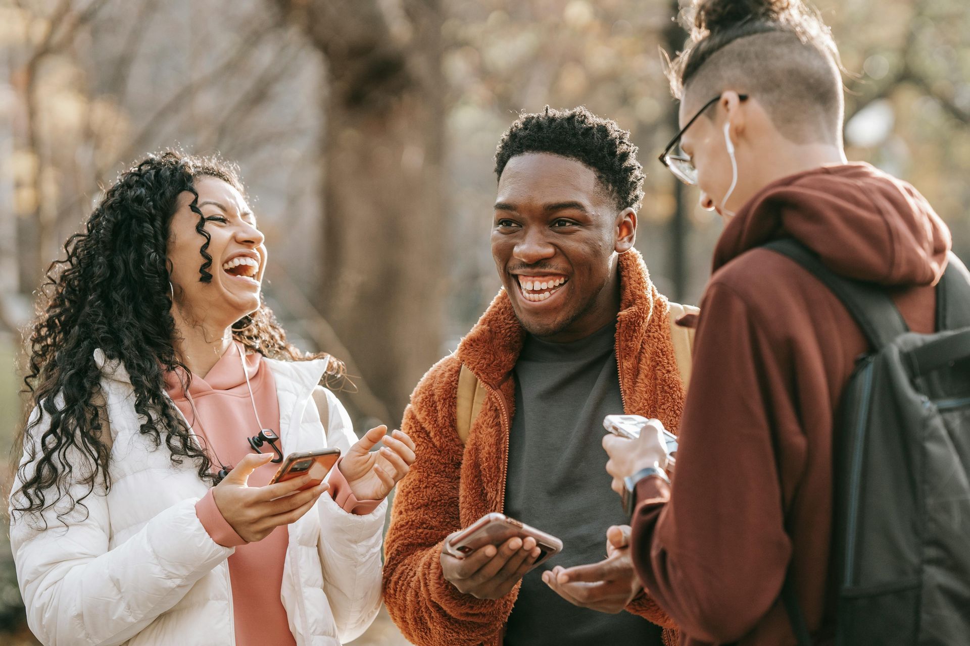 A group of young adults are laughing and looking at their phones.