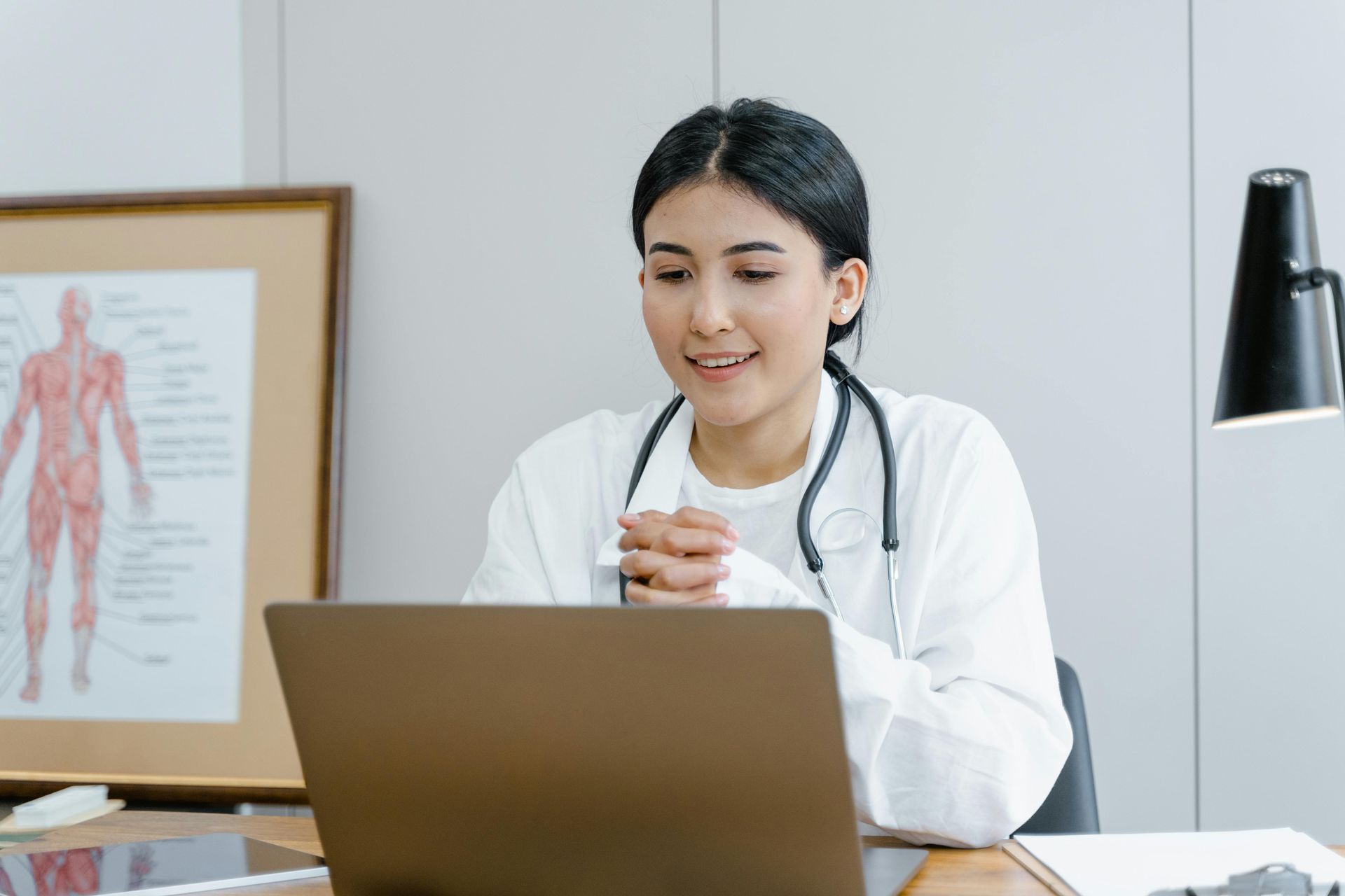 A female doctor is sitting at a desk using a laptop computer.