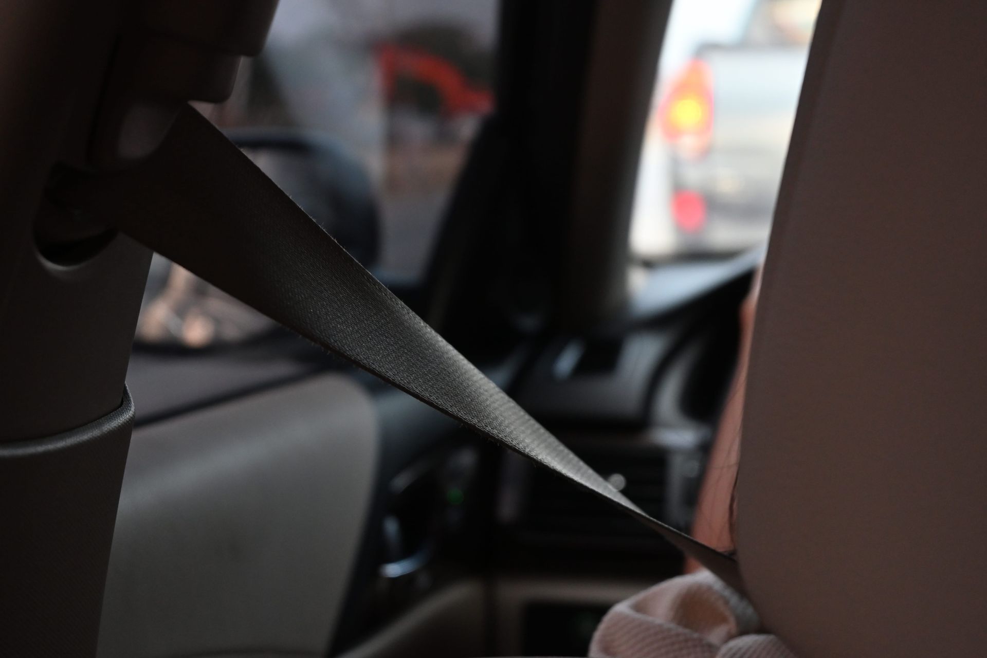 Hand holding a black seat belt strap inside a car, with blurred traffic outside