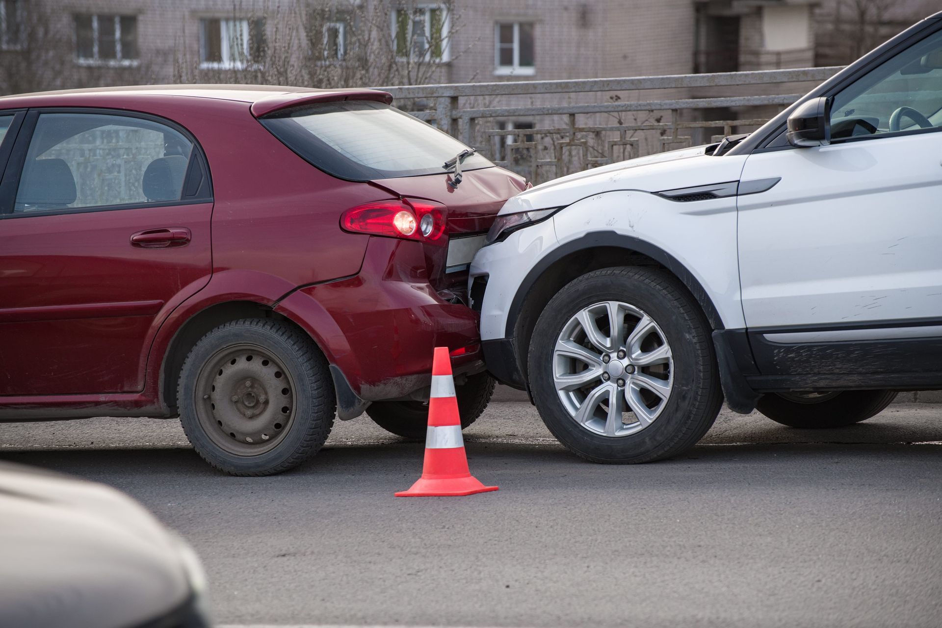 Red car rear-ended by white SUV in a road collision, with an orange cone marking the crash scene.