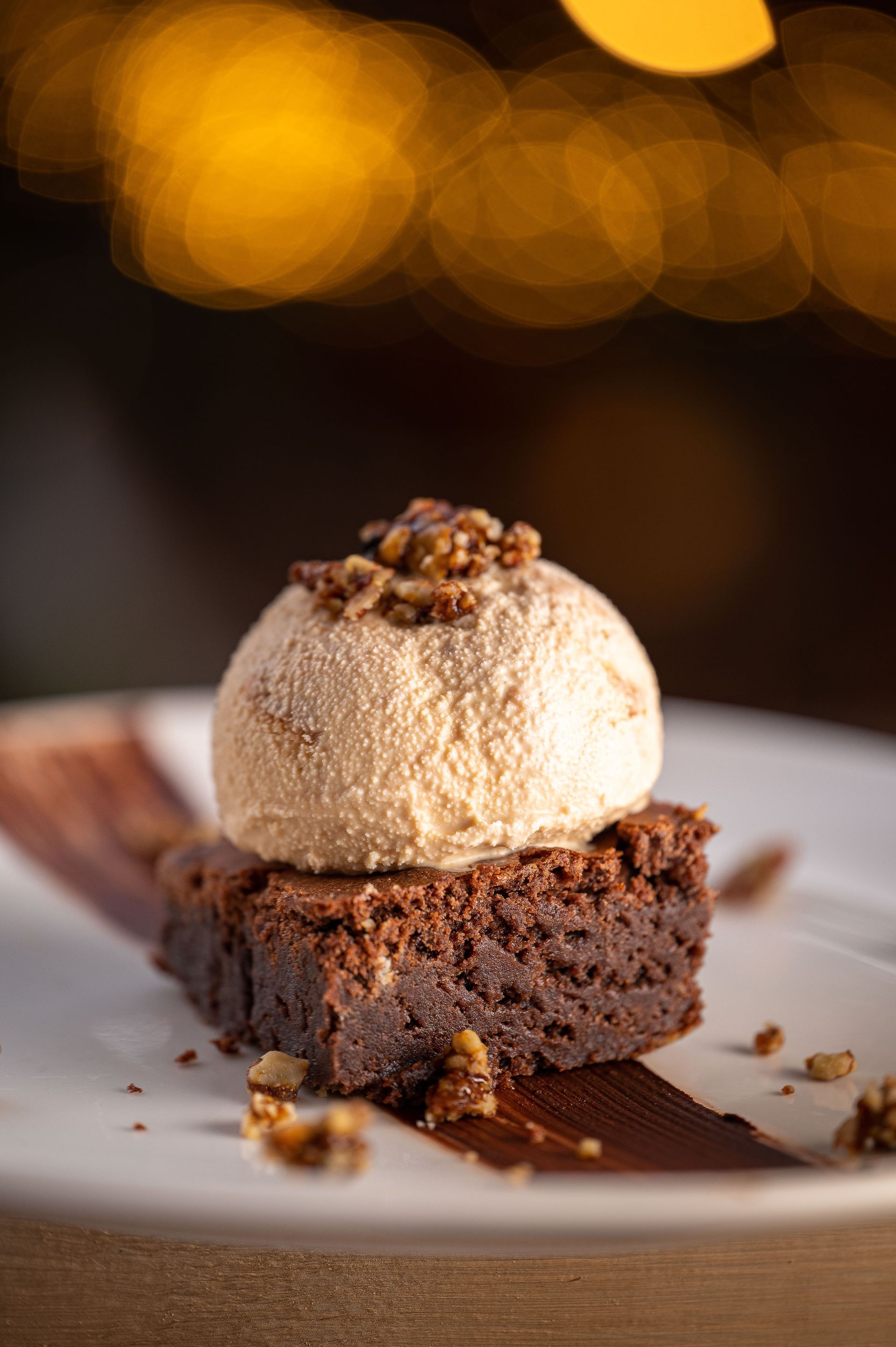 Un brownie con helado encima en un plato blanco.
