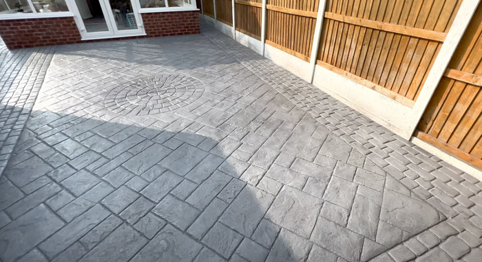 A picture of a stamped concrete patio with a wood fence and back of a house.