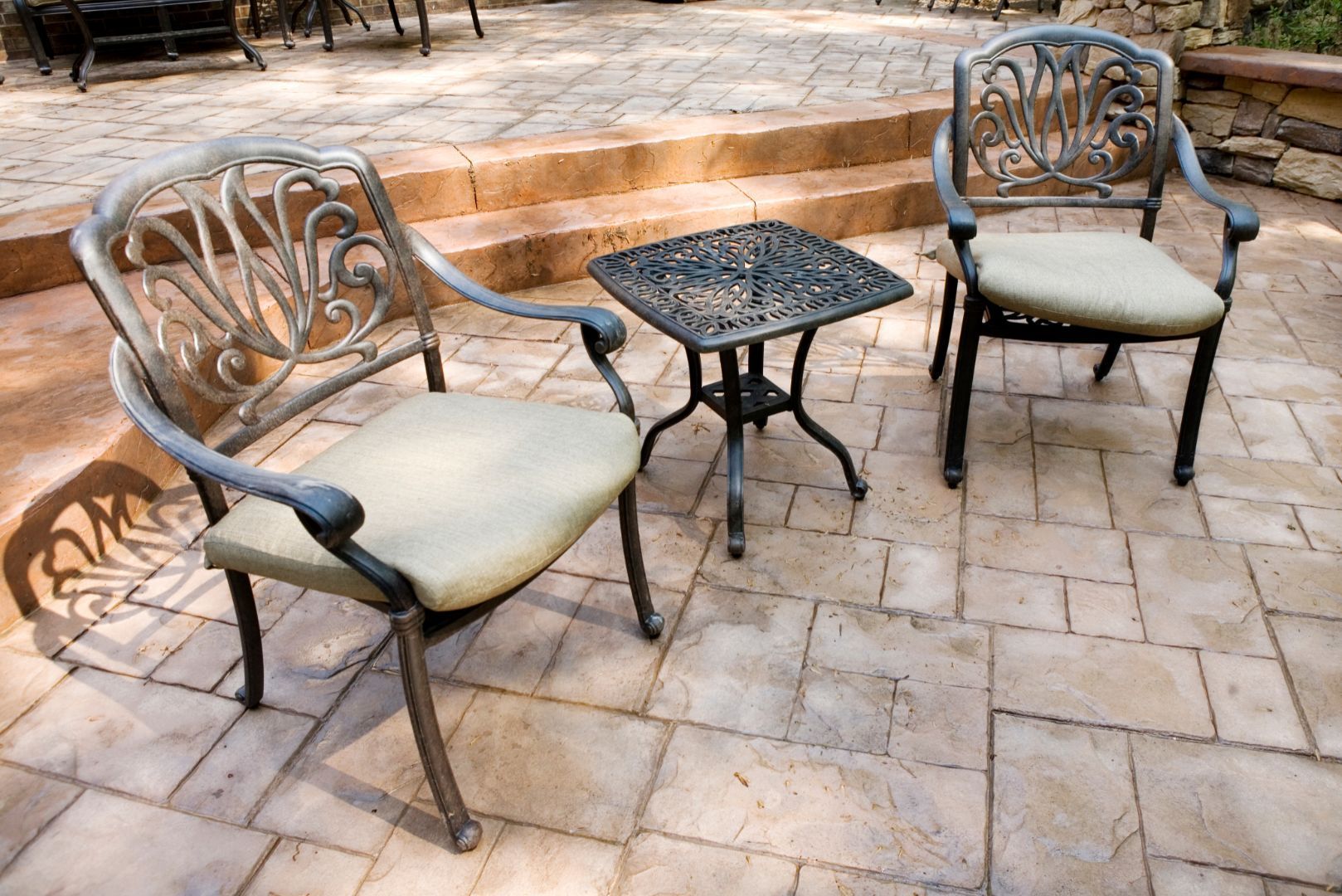 an image of a stamped concrete patio with chairs, a side table, and steps