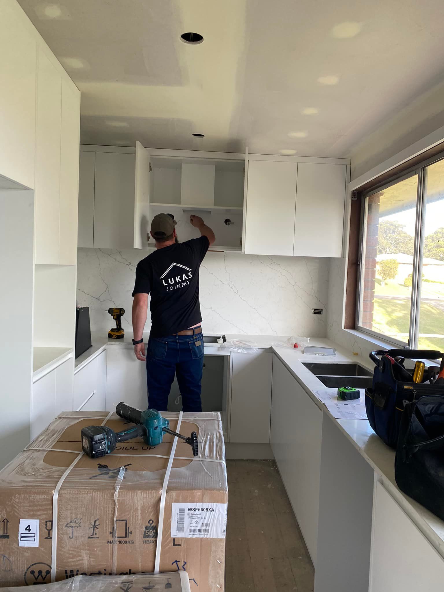 Man Installing Kitchen Cabinets in A White Kitchen  — Lukas Joinery in Belmont, NSW