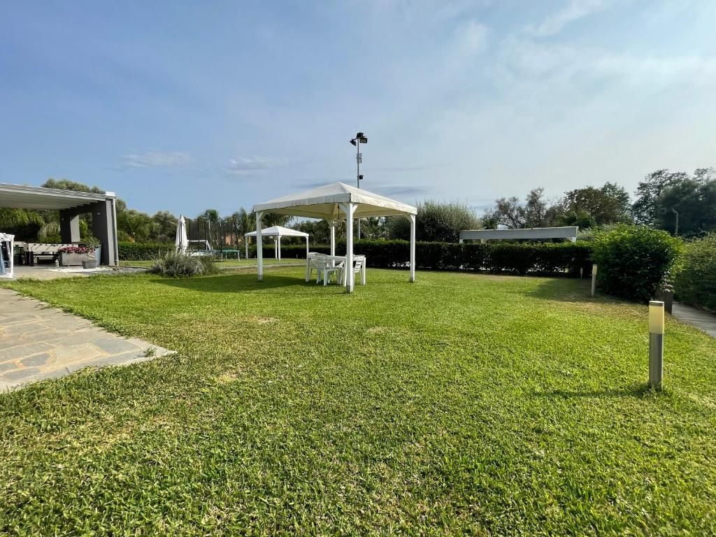 Un grande prato con una tenda bianca e delle sedie.