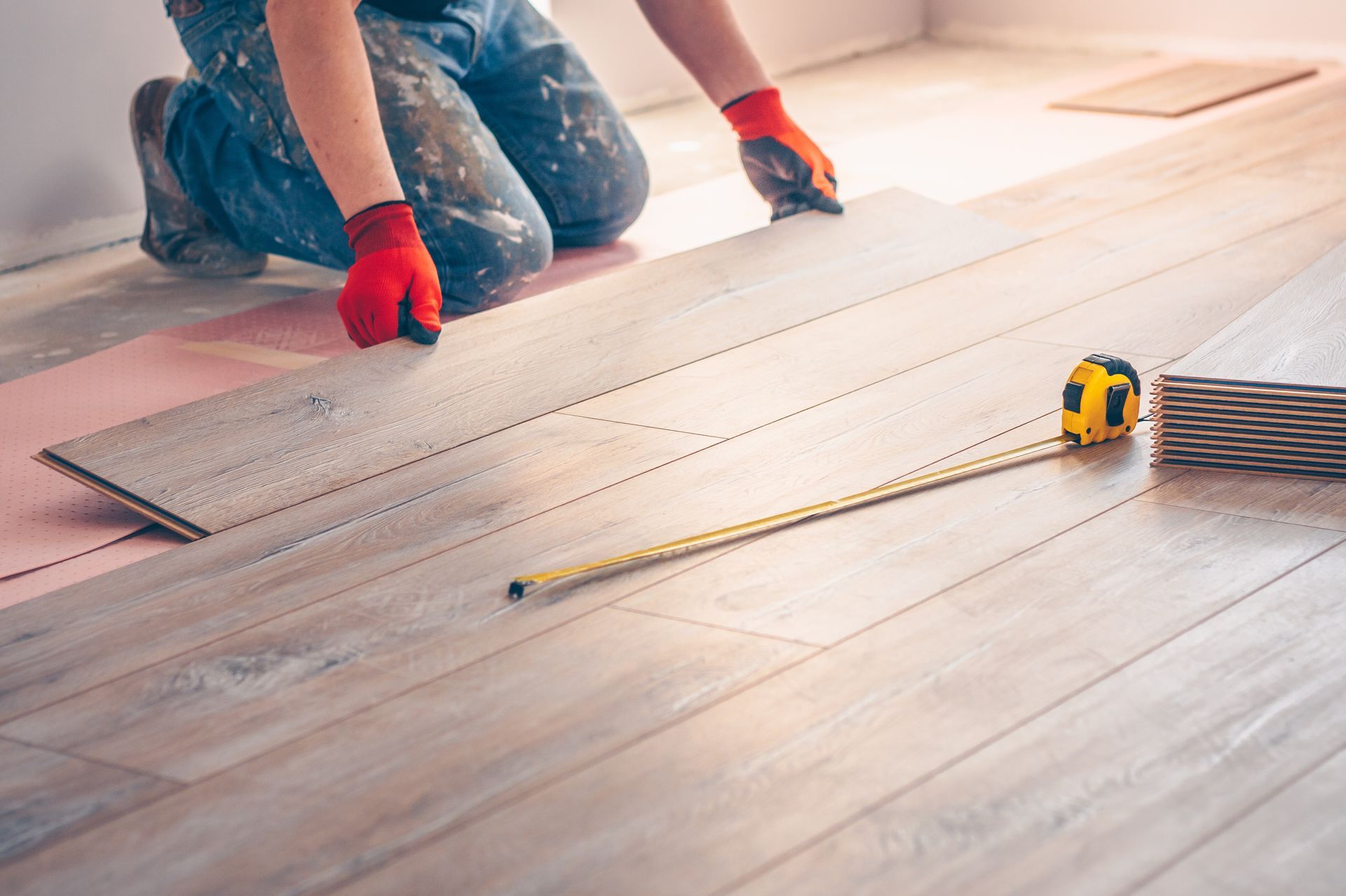 A man is installing a wooden floor with a tape measure.