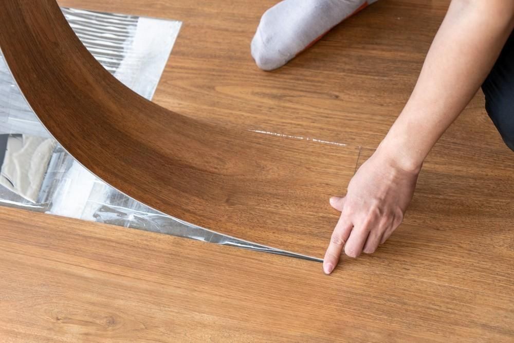 A person is laying a piece of wood on a wooden floor.