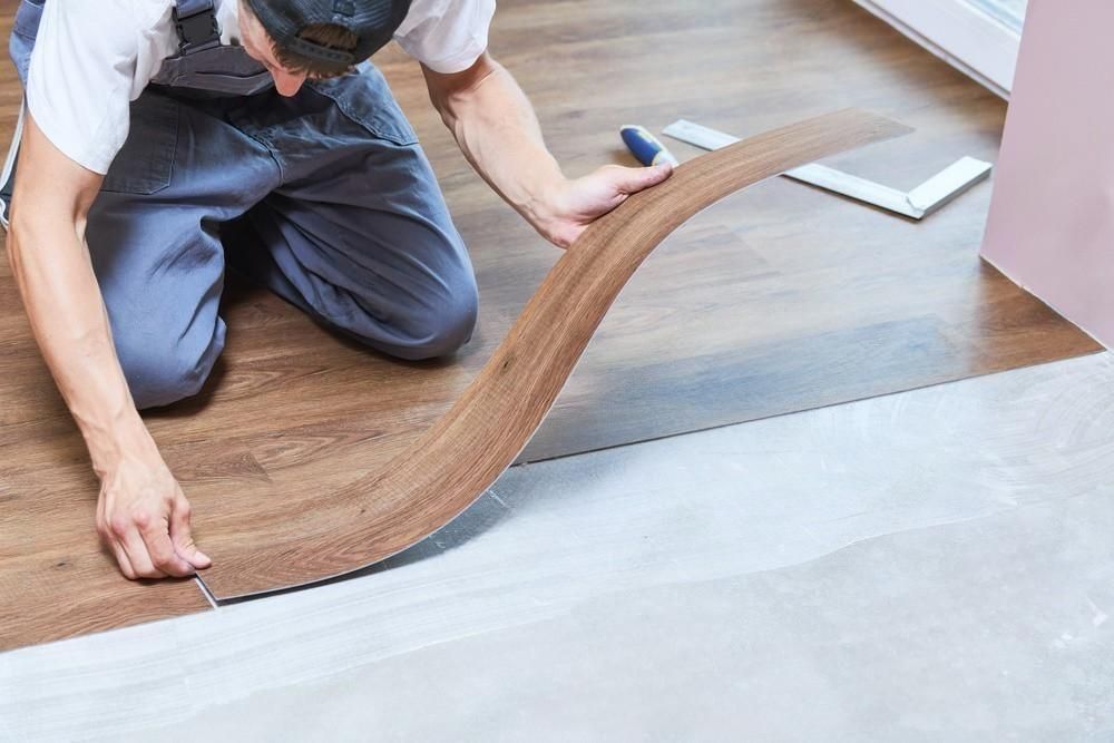 A man is kneeling on the floor while installing a wooden floor.