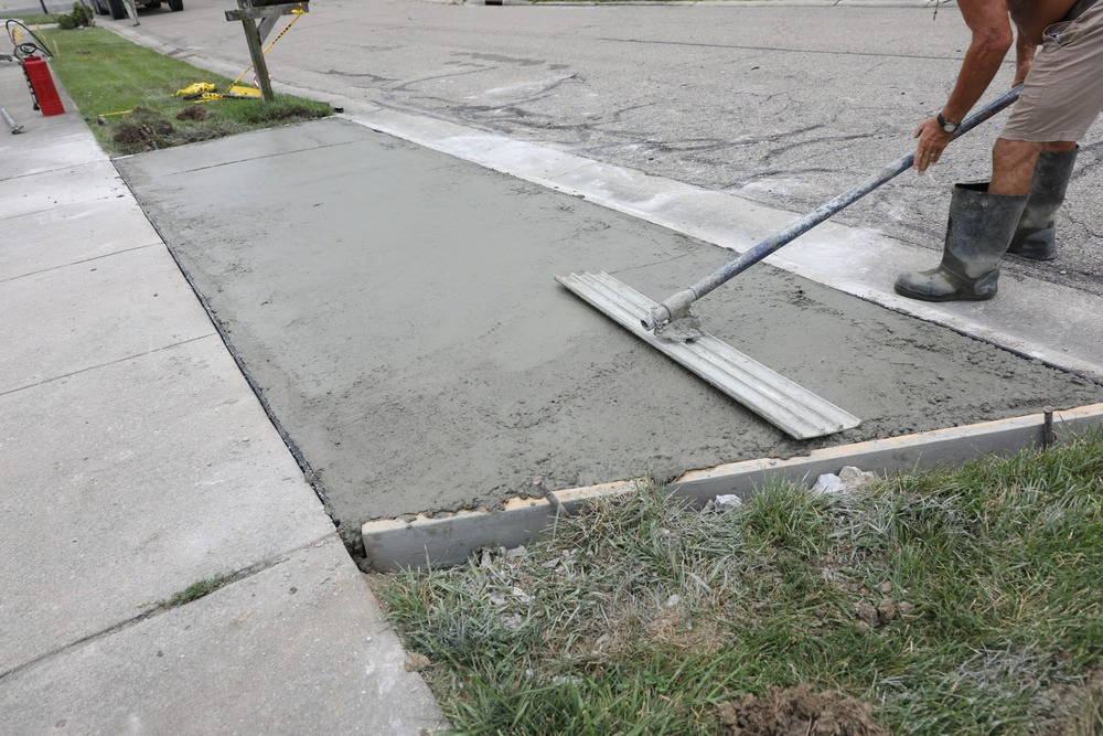 A man is spreading concrete on a sidewalk with a broom.