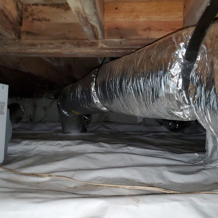 View of crawlspace with HVAC ducting, white vapor barrier, and wooden beams.