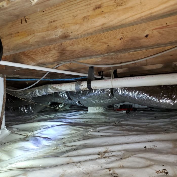 Under-house view: insulation, ductwork, pipes, and wiring against wooden beams.