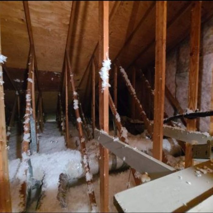 Attic with wooden beams, insulation, and pipes. Interior shot, dimly lit.