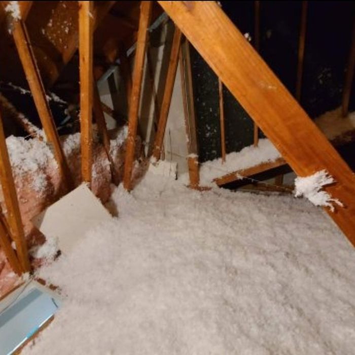 Attic with wood beams, white insulation, and a small window.