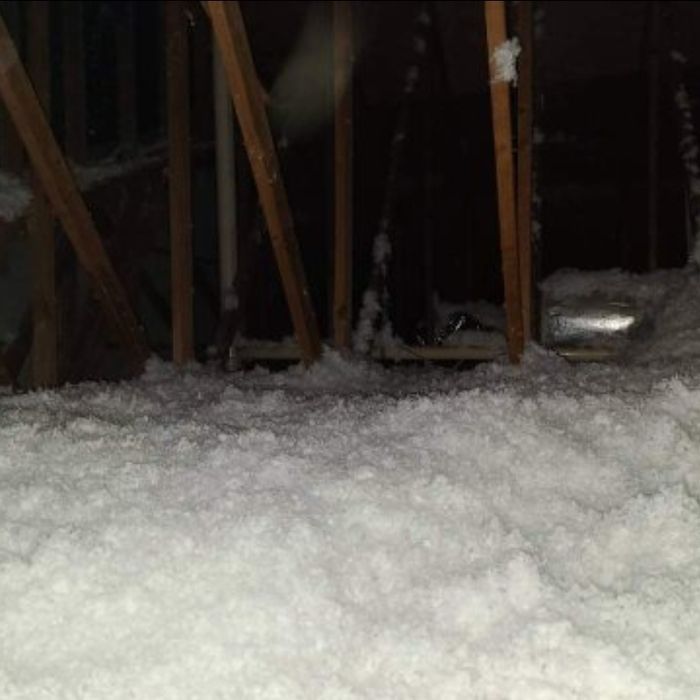 White insulation fills an attic, covering the floor. Wooden beams and dark shadows are visible.
