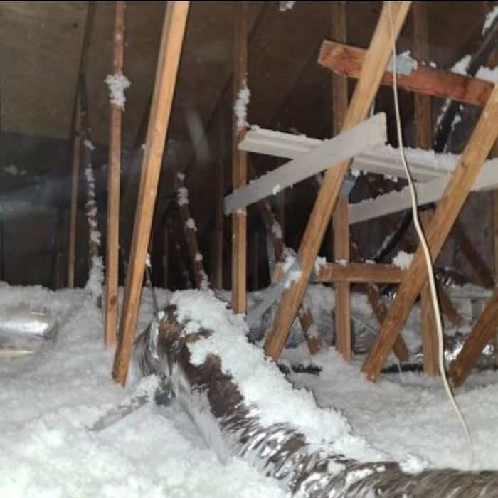Attic space with insulation, wooden beams, and a silver duct.