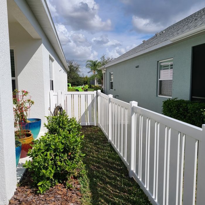 White picket fence separating two houses with green grass and cloudy sky.