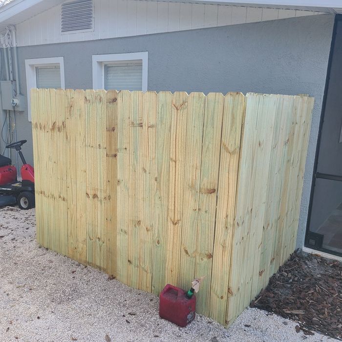 Wooden fence corner next to a gray building with a gas can on gravel.