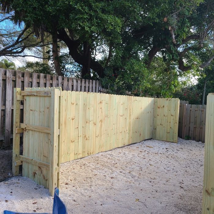 Wooden fence encloses a sandy area, with trees in the background.