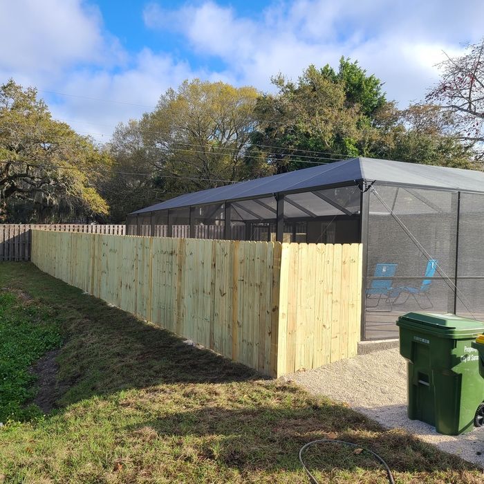 Wooden fence alongside a backyard pool with a screened enclosure and green trash can.