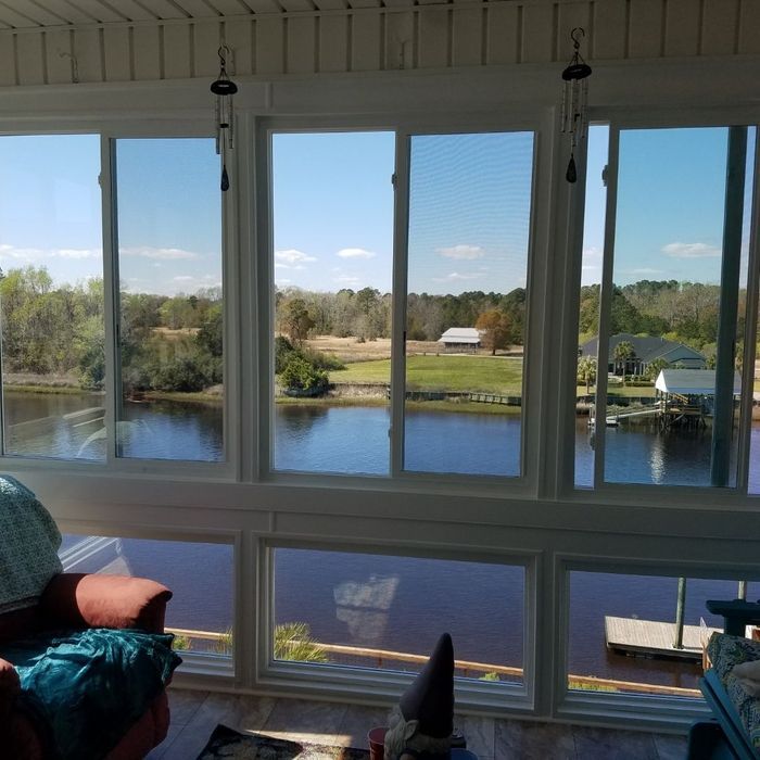 Sunroom with view of a river, trees, and blue sky. A few chimes hang.