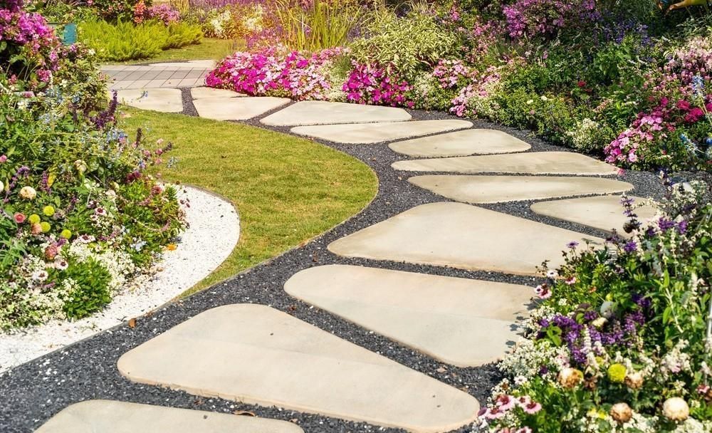 a stone walkway in a garden surrounded by flowers and grass .