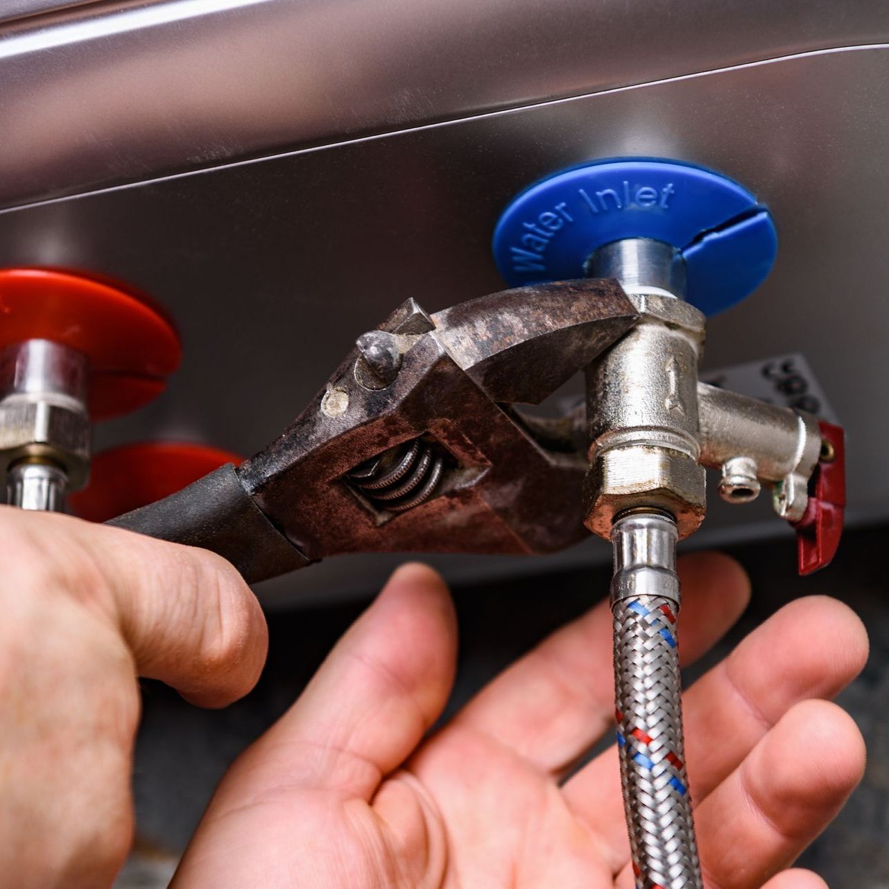 A person is fixing a water heater with a wrench.