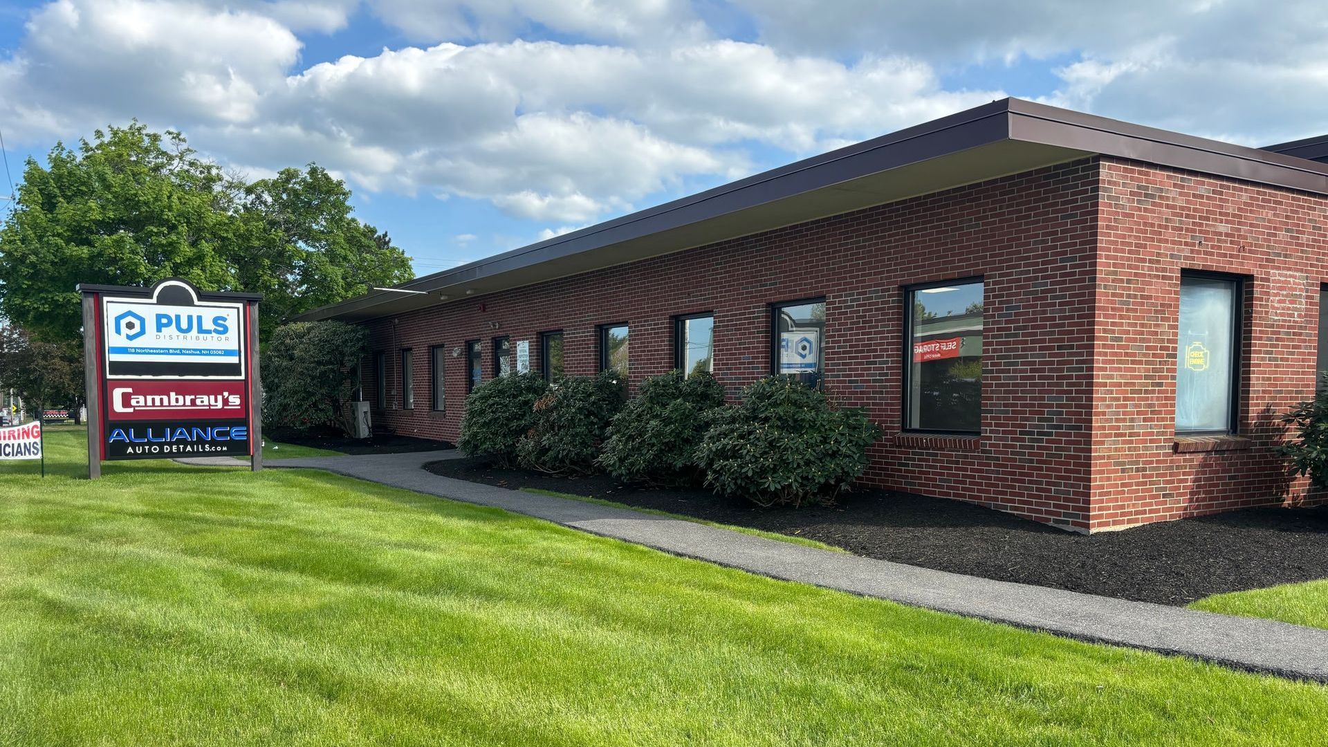 Brick office building with a sign on a green lawn under a partly cloudy sky.