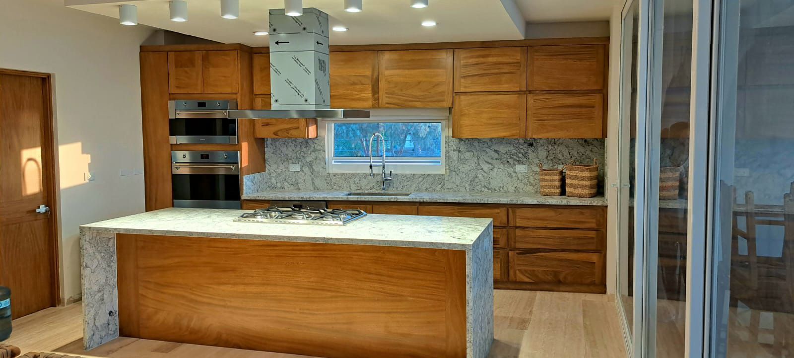 Una cocina con gabinetes de madera , sobres de granito , electrodomésticos de acero inoxidable y una gran isla.
