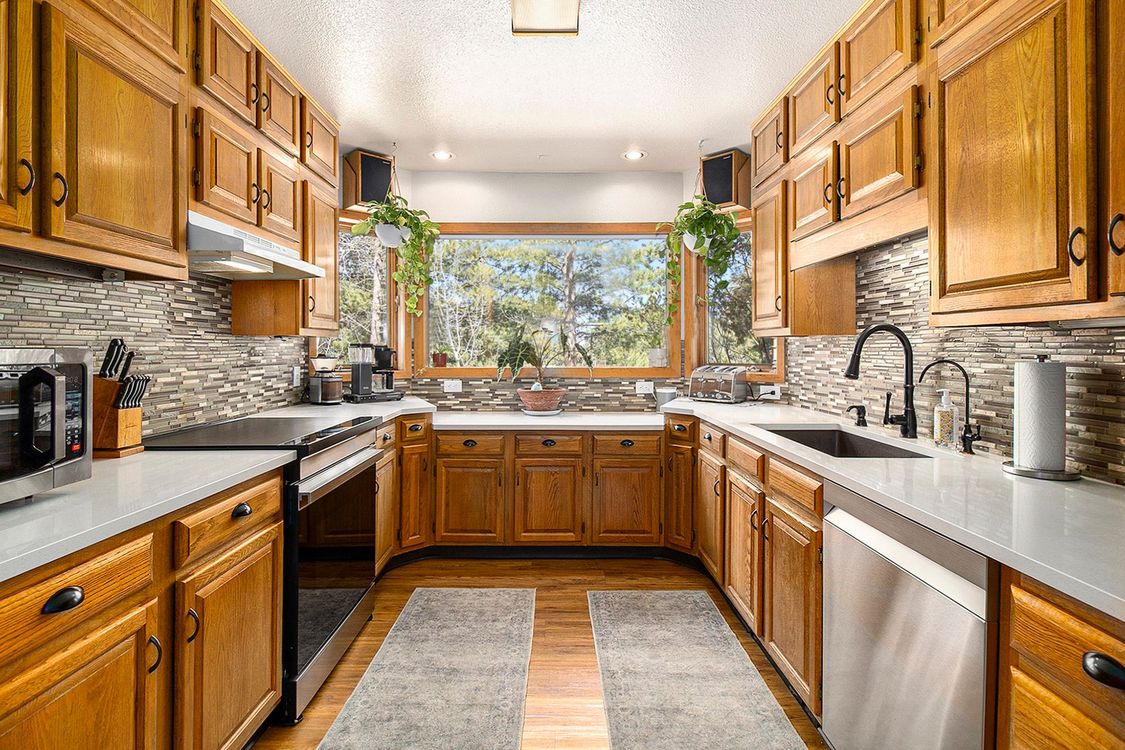 A kitchen with wooden cabinets , stainless steel appliances , and a large window.