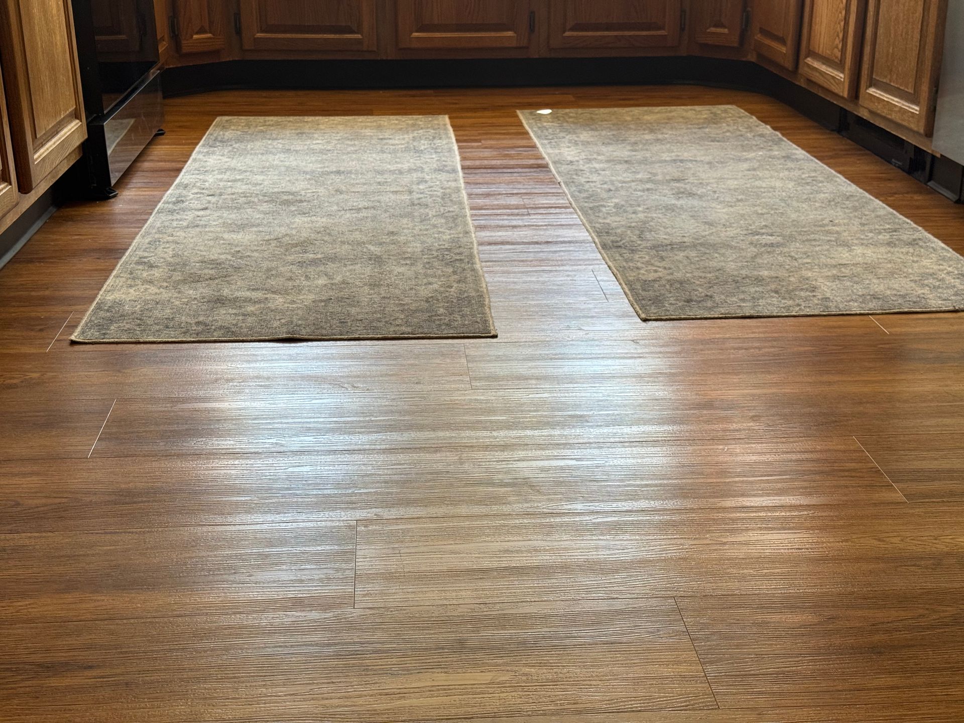 Two rugs are sitting on a wooden floor in a kitchen.