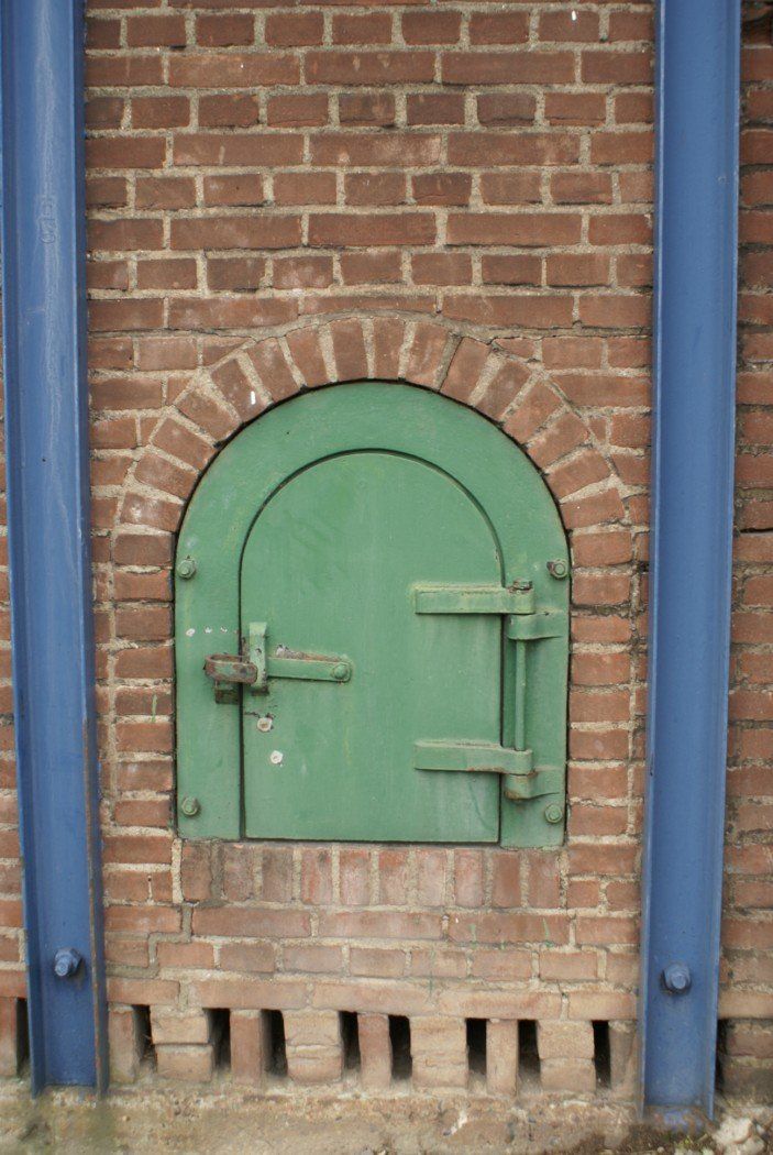 Groene boogdeur in een rode bakstenen muur, met blauwe leidingen aan weerszijden.