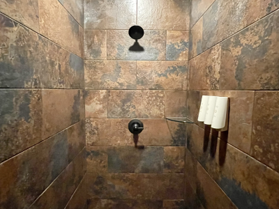 A shower with brown and gray stone-like tiles, black showerhead and controls, and white shampoo bottles.