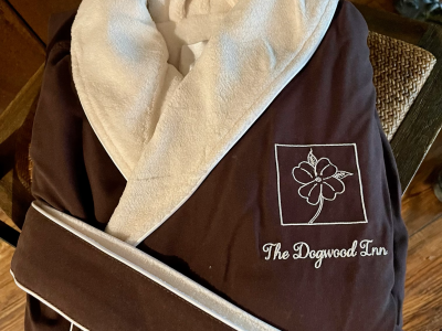 Brown bathrobe with white trim, folded on a wooden surface. The logo for 