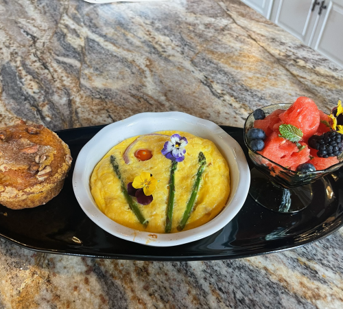 Breakfast plate with a muffin, egg dish decorated with flowers, and fruit salad.