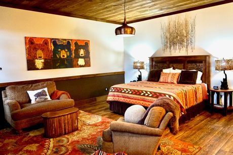 Bedroom with a bed, lamps, and decorative wall art. Warm colors, wood furniture, and patterned bedspread.