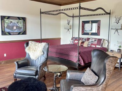 A rustic bedroom with a four-poster bed, two leather armchairs, and a small side table. 