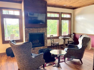 Cozy living room with fireplace. Brown chairs, a small table, and a rug are arranged around the fireplace.